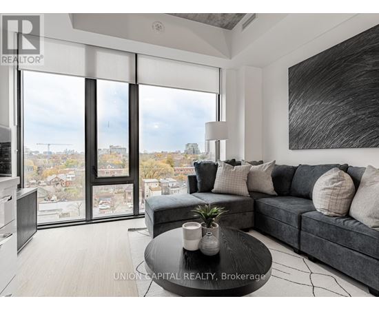 A modern living room with a grey couch and a large window overlooking a cityscape.