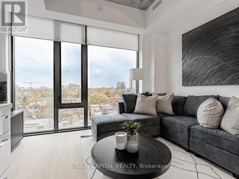 A modern living room with a grey couch and a large window overlooking a cityscape.