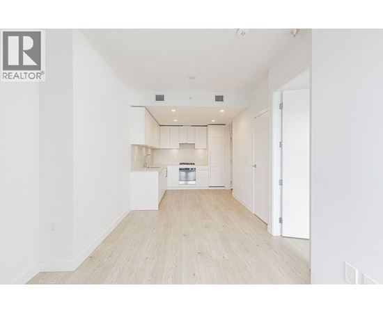 A spacious, empty room with a kitchen area in the background.