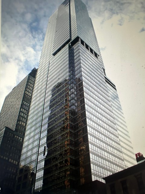 A tall skyscraper with a glass facade stands in front of a cloudy sky.