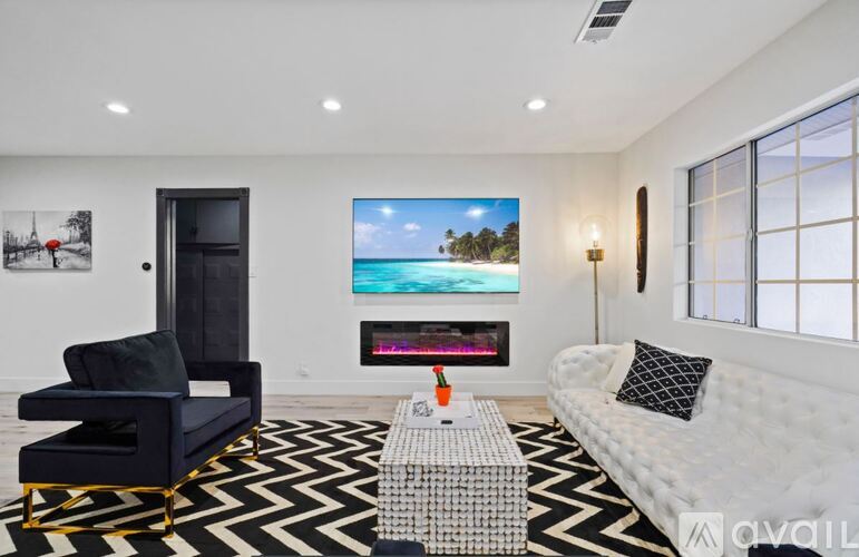 A modern living room with a black and white chevron rug, a black chair, a white sofa, and a large painting of a beach scene on the wall.