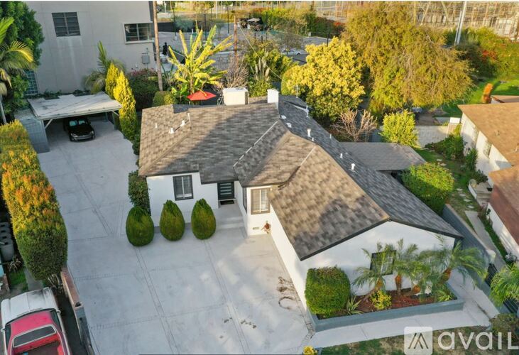 A house with a grey roof and a white wall surrounded by green trees.