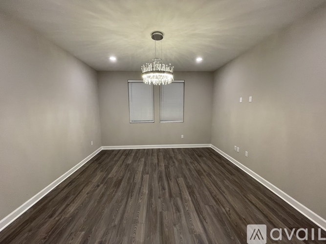 A spacious room with wooden flooring and a chandelier hanging from the ceiling.