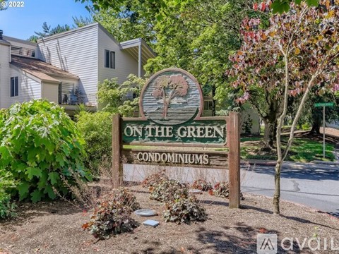 A sign for On the Green Condominiums is in front of a tree and houses.