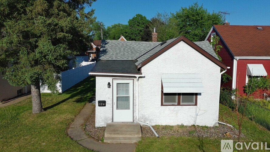 A small white house with a black roof and a red house in the background.