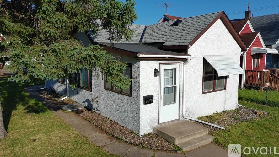 A small white house with a grey roof and a red roofed house in the background.