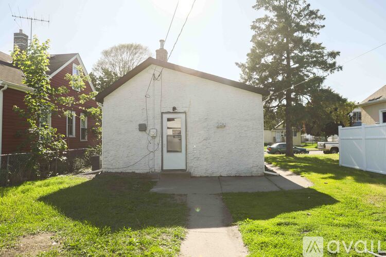 A small white building with a door is surrounded by a green lawn.