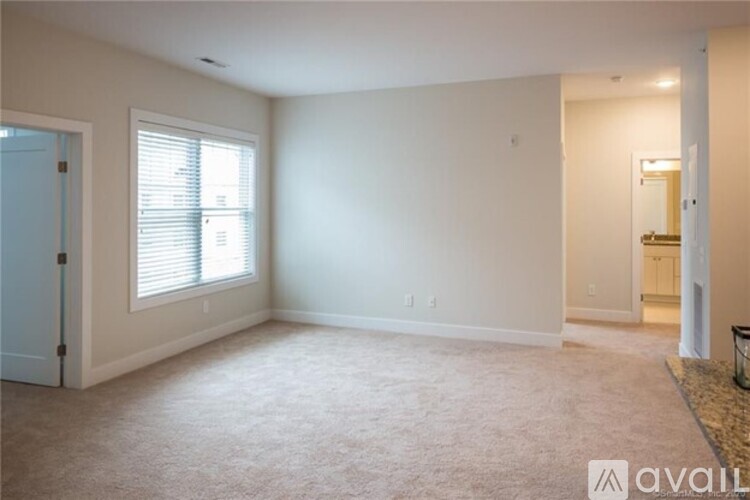 A spacious living room with a carpeted floor and a window with blinds.