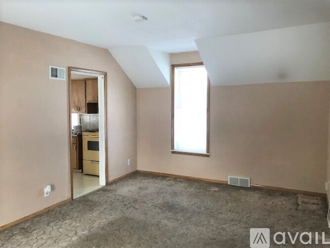 A room with beige walls and a carpeted floor with a window letting in natural light.