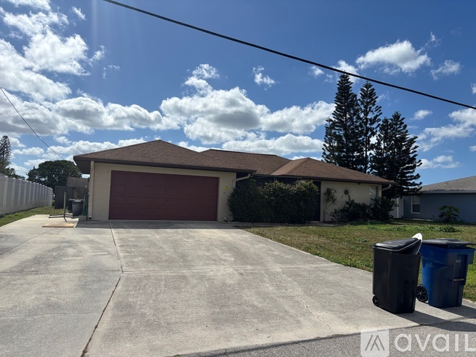 A house with a brown garage door and a blue and black trash can in front of it.