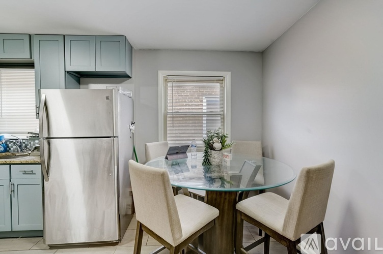 A kitchen with a glass table and chairs, a refrigerator, and a window with blinds.