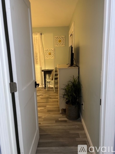 A hallway with a door on the left and a chair and table in the background.