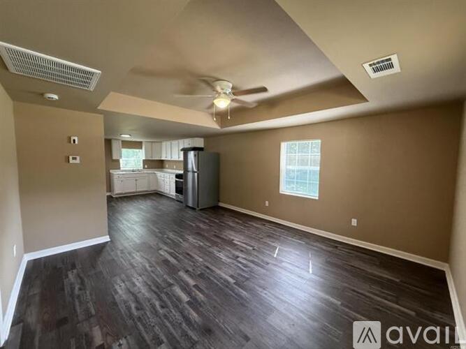A spacious living room with a kitchen in the background and hardwood floors.