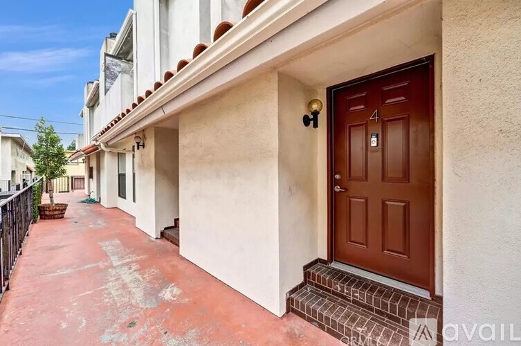 A brown door with the number 4 on it is on the right side of a white building.