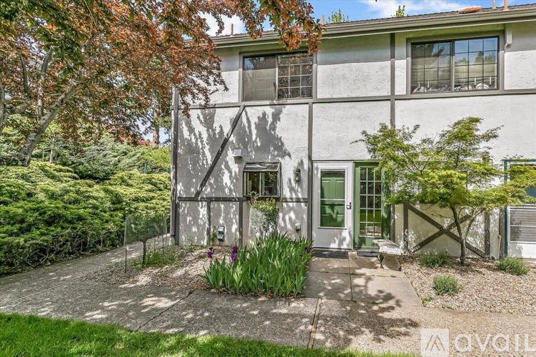 A house with a grey facade and a green door surrounded by a garden.