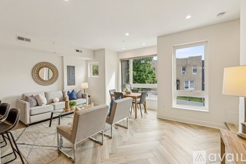 A living room with a grey sofa, a wooden floor, and a large window overlooking a building.
