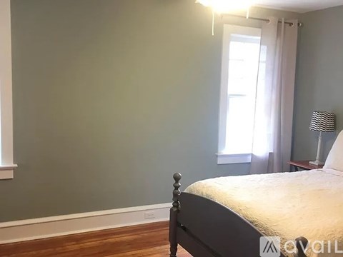 A bedroom with a bed, a window with curtains, and a lamp on a side table.