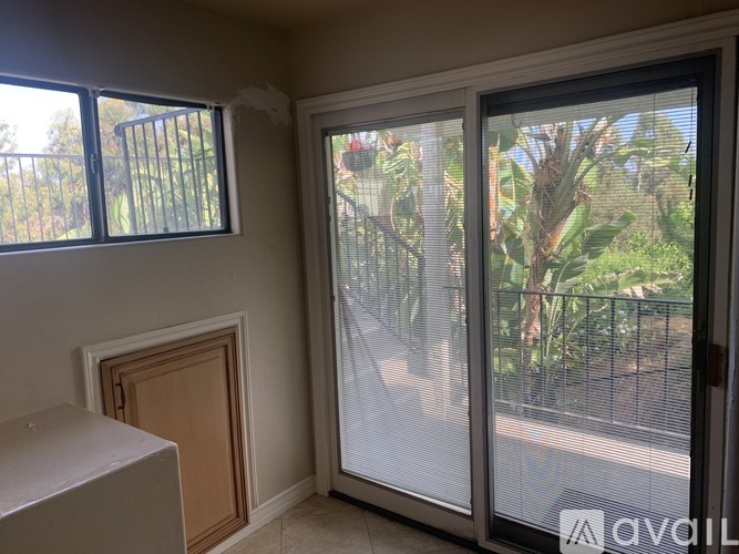 A room with a sliding glass door leading to a balcony with a view of a fence and trees.