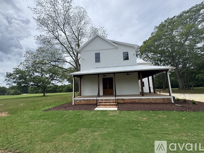 A white house with a porch and a brown door is surrounded by green grass.