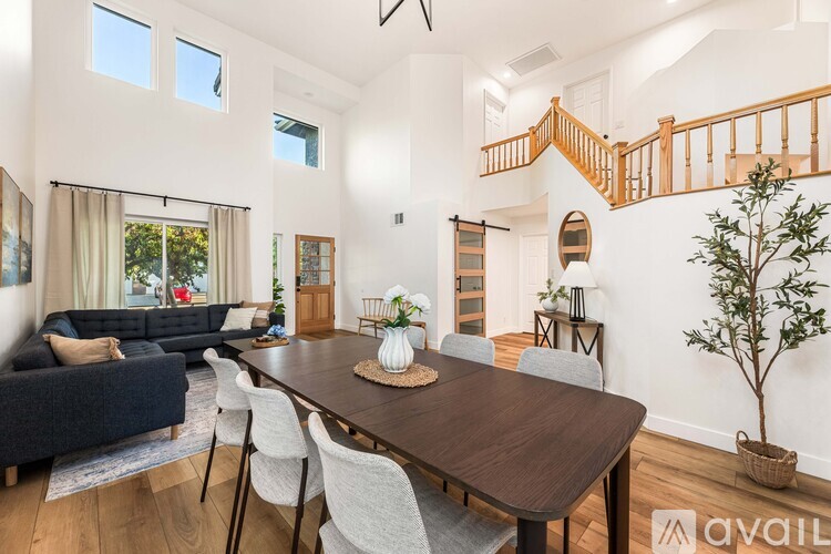 A dining room with a wooden table and chairs, a sofa, a staircase, and a tree.