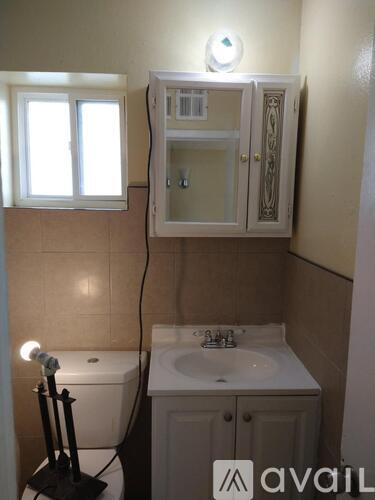 A bathroom with a toilet, sink, and a cabinet with a mirror above it.
