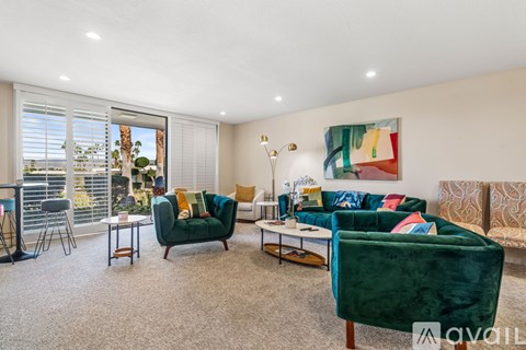 A living room with a green velvet sofa and a painting on the wall.