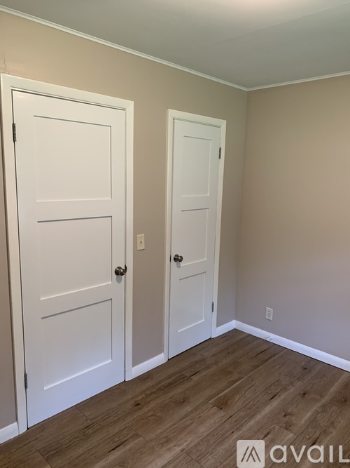 Two white doors in a room with wooden floors.