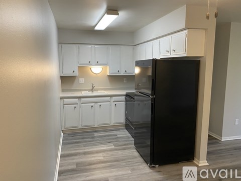 A black refrigerator stands in a kitchen with white cabinets.