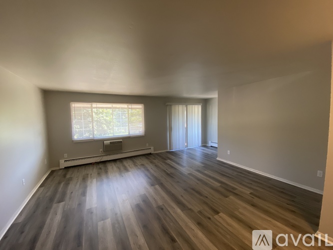A room with wooden flooring and a window with white curtains.