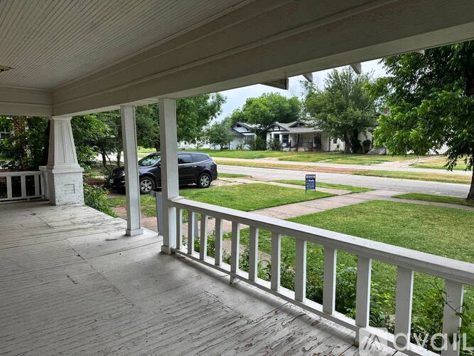 A porch with a white railing and a black car in the background.