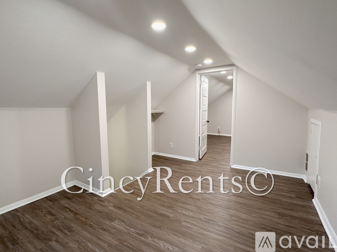 A spacious room with wooden flooring and white walls, with a staircase leading to another level.
