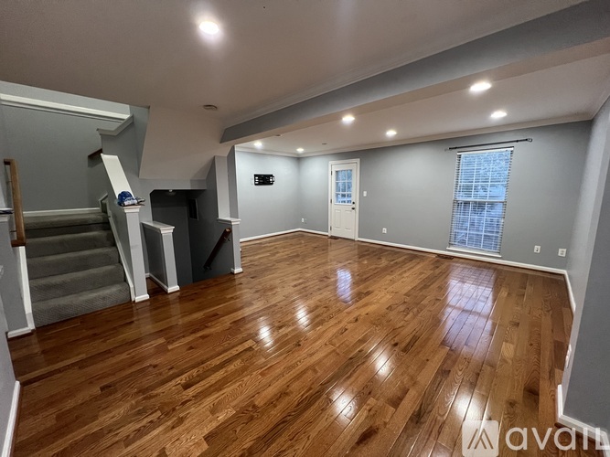 A spacious room with wooden flooring and a staircase.