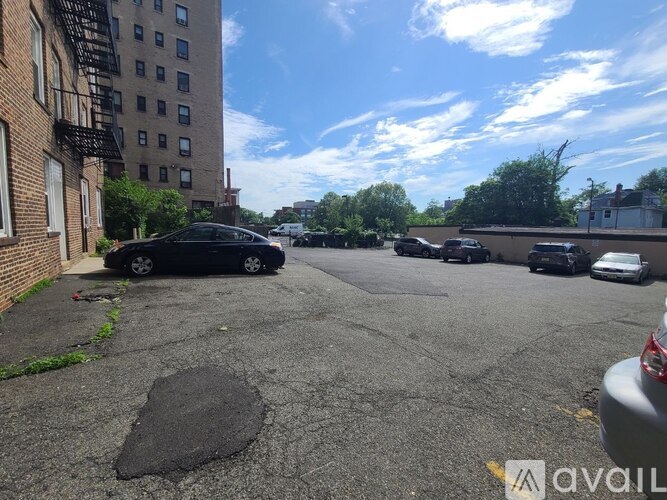 A black car is parked in a parking lot with a large pothole in the foreground.