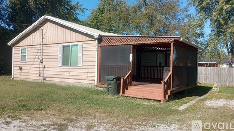 A small house with a deck and a green trash can.