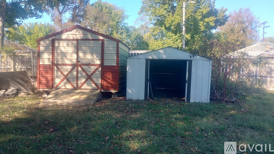 Two sheds, one red and one white, are situated in a grassy area.