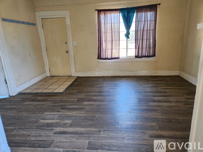 A room with wooden flooring and a window with curtains.