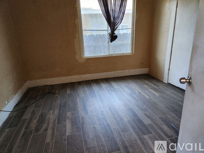 A room with wooden flooring and a window with a curtain.