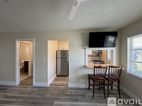 A kitchen with a refrigerator, a television, and a dining table with chairs.