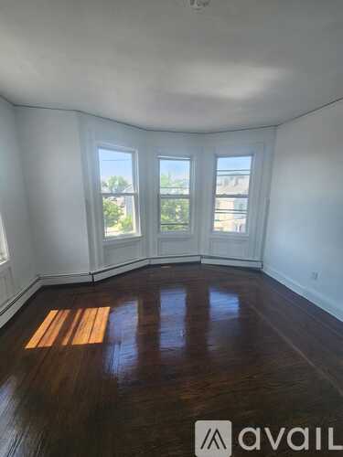 A room with wooden floors and white walls has a window with a view of a building.