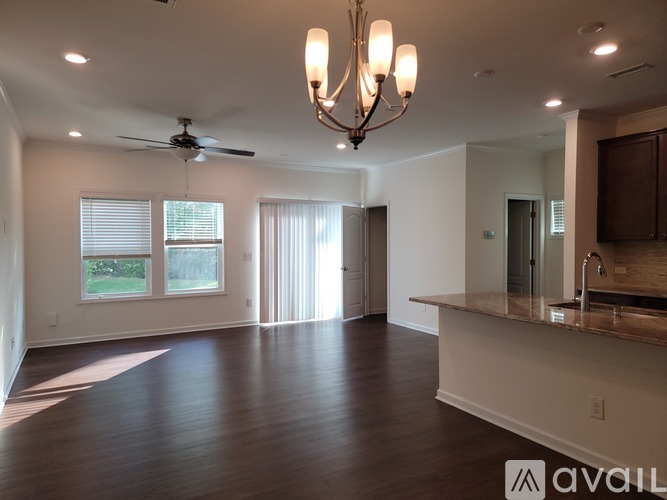 A spacious room with a chandelier, ceiling fan, and a kitchen area with a sink and cabinets.