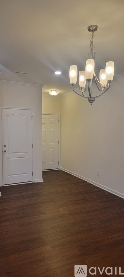 A chandelier hangs from the ceiling in a room with wooden floors and white walls.