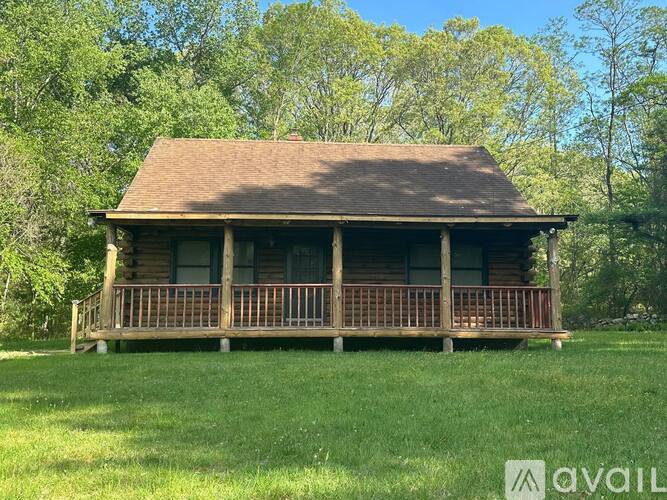 A wooden house with a porch is surrounded by greenery.