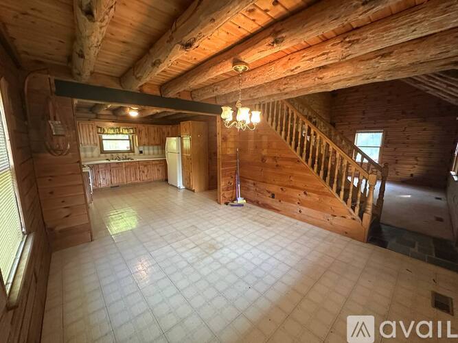 A spacious room with wooden walls and ceiling, a chandelier, and a staircase.
