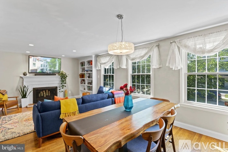 A bright and airy living room with a fireplace, a blue sofa, and a wooden dining table.