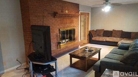 A living room with a brick fireplace and a television on a stand.