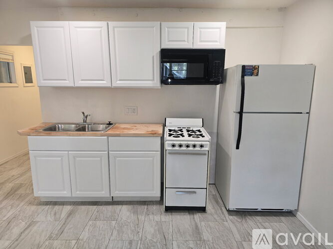 A kitchen with white cabinets, a black microwave, a white stove, and a white refrigerator.