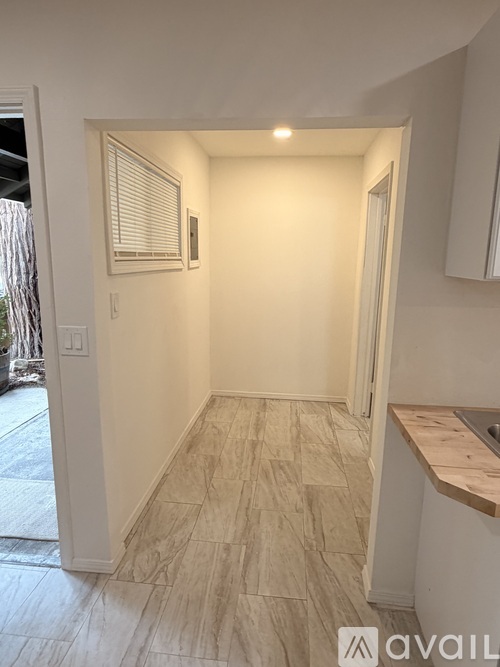 A hallway with a tiled floor and a window with blinds.