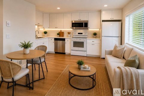 A modern kitchen with white cabinets and appliances, a dining table with chairs, and a living area with a couch.