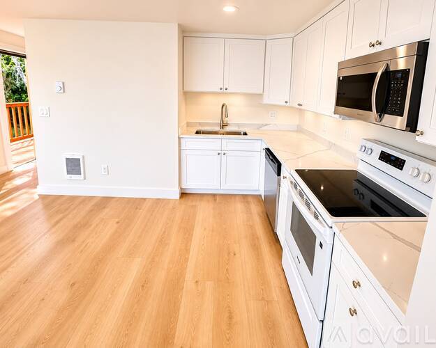 A kitchen with white cabinets and appliances, and wooden flooring.