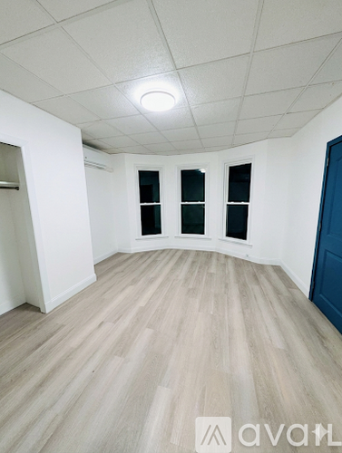 A room with wooden flooring and three windows.